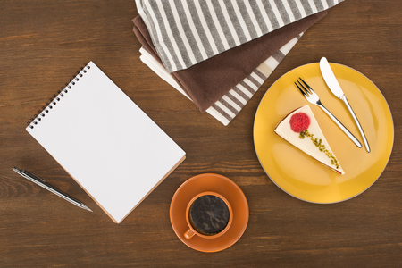 top view of blank notebook with pen, gourmet cake and cup of coffee on wooden tableの写真素材