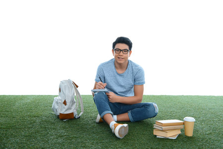 teen asian student boy studying while sitting on grass isolated on whiteの写真素材