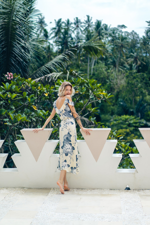 back view of attractive blond woman in dress standing on terrace at villaの写真素材