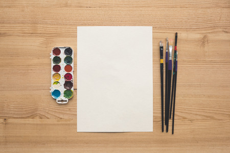 Top view of empty sheet of paper with watercolor paints and brushes