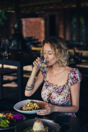 portrait of woman drinking water while having dinner in cafeの写真素材