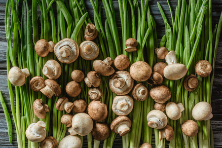 top view of raw champignon mushrooms on green leeks on wooden tabletopの写真素材
