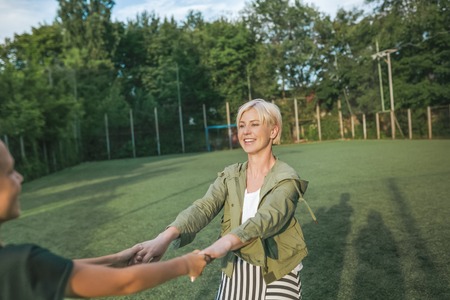 cropped shot of happy mother and son holding hands and having fun on green lawnの写真素材