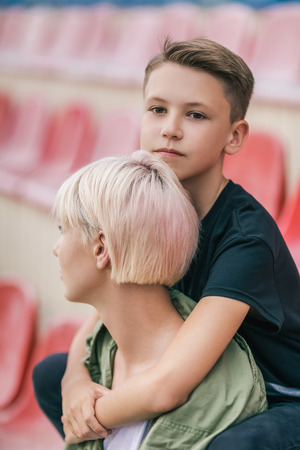 cute pensive boy hugging mother and looking at camera on stadiumの写真素材