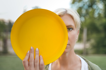 beautiful blonde woman holding yellow flying disk and looking at camera