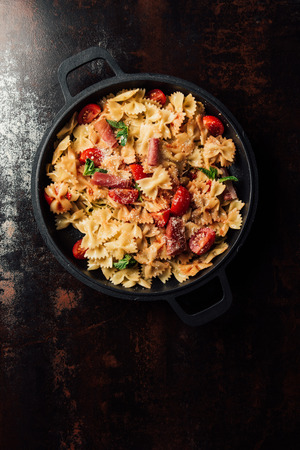 top view of pasta with jamon, cherry tomatoes, mint leaves covered by grated parmesan in pan on tableの写真素材