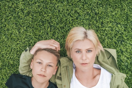 top view of beautiful mother and son looking at camera while lying together on green grassの写真素材