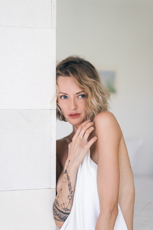 portrait of tender blond woman covering body white bedsheetの写真素材