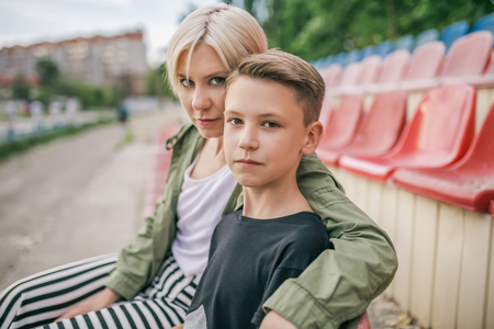 beautiful mother and son looking at camera while sitting together on stadium seatsの写真素材