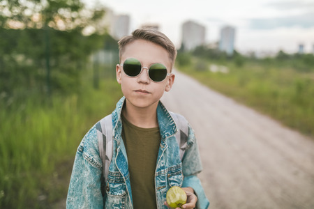 cute boy in sunglasses and denim jacket holding apple and looking at cameraの写真素材