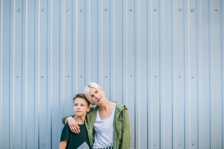 beautiful stylish mother and son looking away while standing and embracing on streetの写真素材