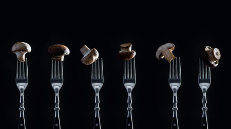 row of champignon mushrooms on forks isolated on blackの写真素材