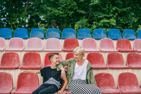 happy mother and son smiling each other while sitting together on stadium seatsの写真素材