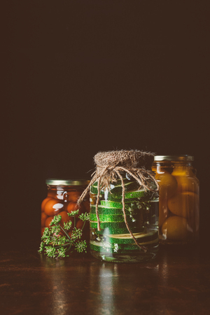 glass jars with preserved vegetables on wooden table in dark kitchenの写真素材
