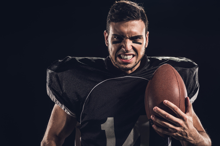 close-up portrait of angry american football player with ball looking at camera isolated on blackの写真素材