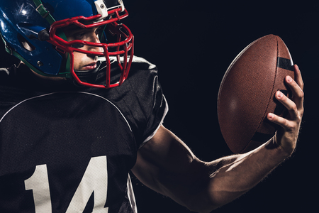 close-up portrait of equipped american football player with ball isolated on blackの写真素材