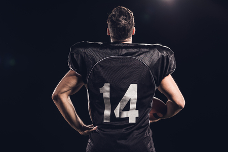 rear view of american football player with helmet in hand isolated on blackの写真素材