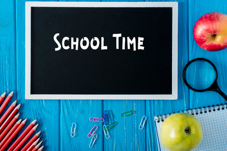 top view of blackboard with lettering school time, apples and stationery on blue wooden backgroundの写真素材