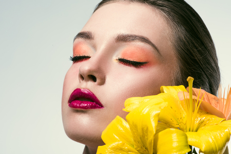 close-up portrait of beautiful young woman with fashionable makeup and yellow lilium flowers  isolated on whiteの写真素材