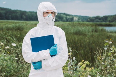 selective focus of female scientist in protective suit and googles holding clipboard in meadowの写真素材