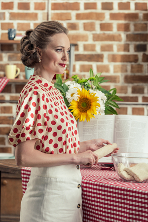 side view of beautiful adult housewife with rolling pin looking away during dough preparation at kitchenの写真素材