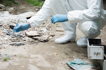 cropped image of male scientist in latex gloves taking sample of stone by tweezers outdoors