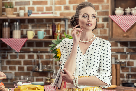 thoughtful adult housewife in vintage clothes looking away at kitchen