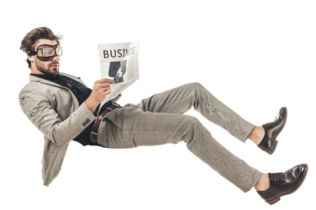 handsome young businessman in vintage aviation goggles reading newspaper while falling isolated on whiteの写真素材