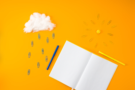 top view of blank notebook and cloud with sun made of paper clips and cotton on yellowの写真素材