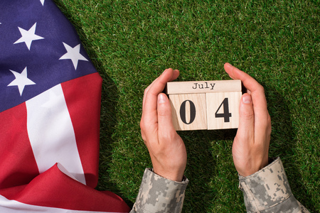 cropped shot of soldier in military uniform holding calendar with 4th july date with american flag...