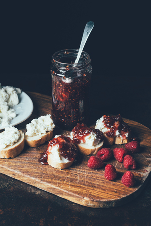 elevated view of raspberries, sandwiches with fruit jam and cream cheese on cutting board on blackの写真素材