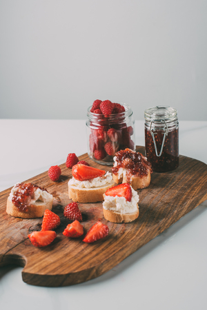 close up shot of cutting board with strawberry jam in jars and sandwiches with cream cheese and jam...