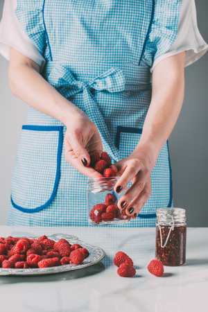 cropped image of woman in apron doing jam from raspberries over tableの写真素材