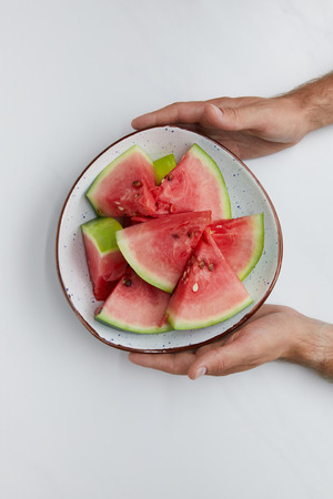 partial view of man holding bowl with watermelon pieces in hands on white surfaceの写真素材