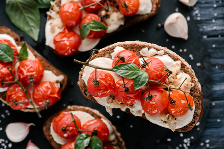 Delicious sandwiches with mozzarella and baked tomatoes on dark wooden tableの写真素材