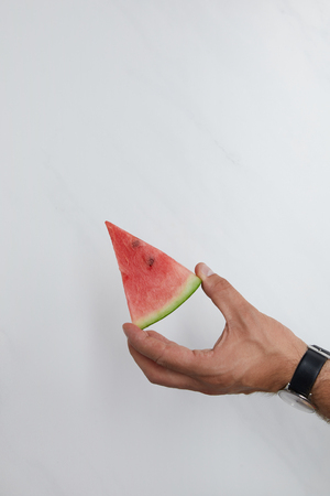 cropped shot of man holding watermelon piece in hands on white surfaceの写真素材