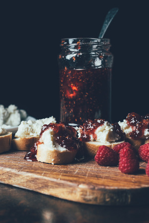 close up view of raspberries, sandwiches with fruit jam and cream cheese on cutting board on blackの写真素材