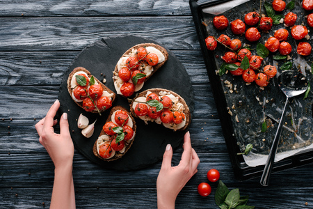 Woman serving sandwiches with cheese and baked tomatoes on dark slate boardの写真素材