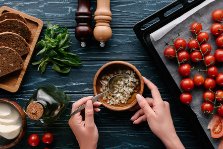 Cropped view of female hands cooking garlic oil on dark wooden table with tomatoes and herbsの写真素材