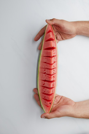 cropped shot of man holding cut watermelon piece in hands on white surfaceの写真素材