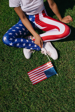 partial view of woman with flagpole in leggins with american flag pattern resting on green lawn, americas independence day holiday conceptの写真素材