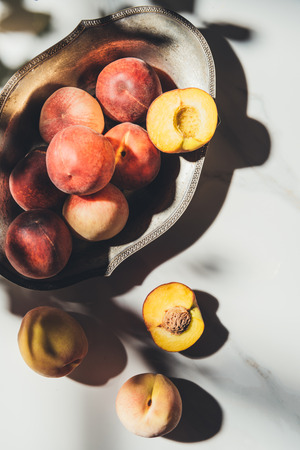flat lay with ripe peaches in metal bowl on light marble surface with shadowsの写真素材