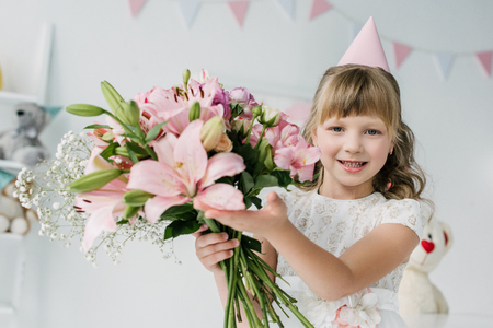 adorable birthday kid in cone showing bouquet of liliesの写真素材