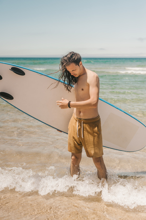 young man with surfboard standing in ocean on summer dayの写真素材