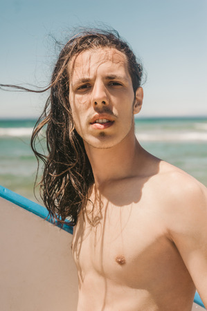 portrait of young man with surfboard with ocean on background on summer day