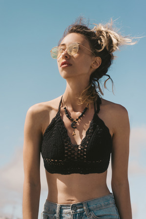 portrait of young stylish woman in sunglasses against blue sky backdropの写真素材