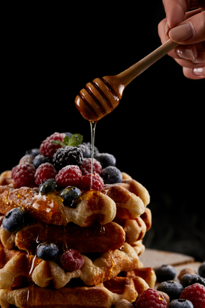 cropped shot of woman pouring honey onto stack of belgian waffles on blackの写真素材