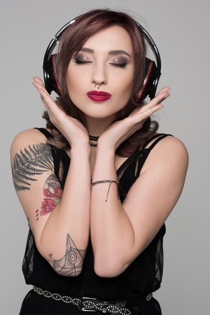 Young woman with tattoos wearing big headphones making a kissing face with her eyes closedの写真素材