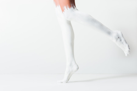 cropped image of girl with legs painted with white paint jumping on white floorの写真素材