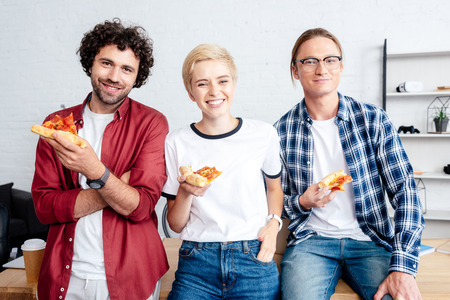 happy young startup team holding pizza and smiling at camera in office